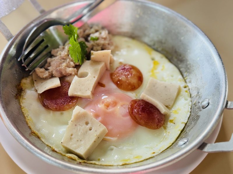 ไข่กระทะร้อน ๆ ใส่กุนเชียง หมูยอ และหมูสับ มีส้อมจิ้มอยู่