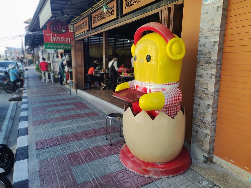 ตุ๊กตาไข่สีเหลืองยืนบนทางเท้าหน้าร้าน