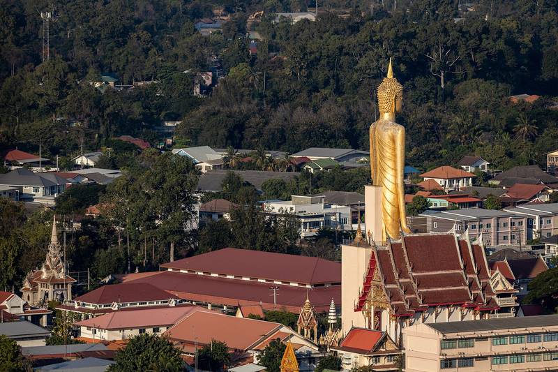 พระพุทธรูปยืนองค์สูงสีทองเหนือหลังคาโบสถ์และบ้านเรือนในเมือง